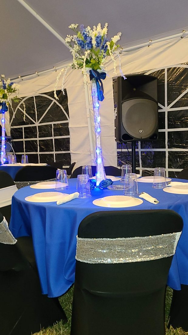 Tent reception with royal blue linens, black chair covers with silver sashes, and tall lit vase centerpieces