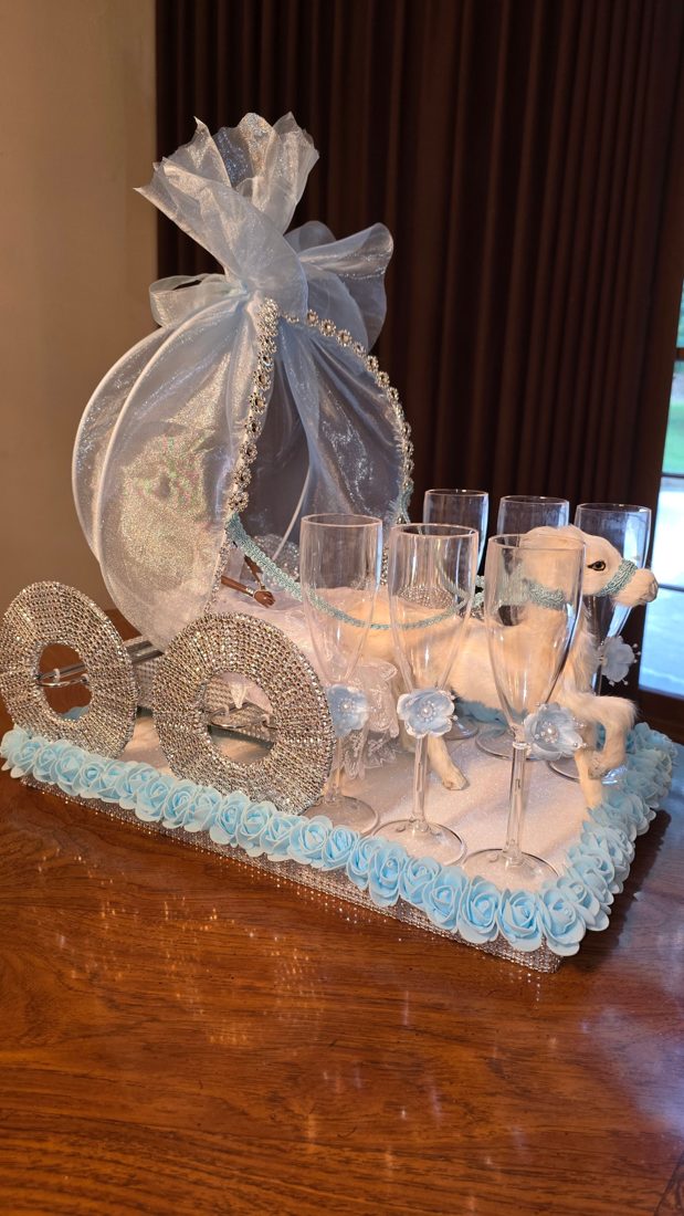 Rhinestone carriage centerpiece with organza canopy, a white horse, champagne flutes, and a border of light blue roses
